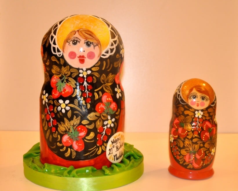 A scale Russian doll cake standing next to an original Russian doll from which it was copied