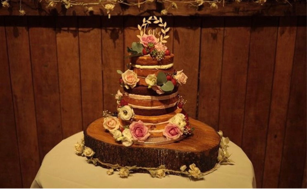 A three tier naked floral cake at Pangdean Barn in brighton with fresh flowers and wooden topper