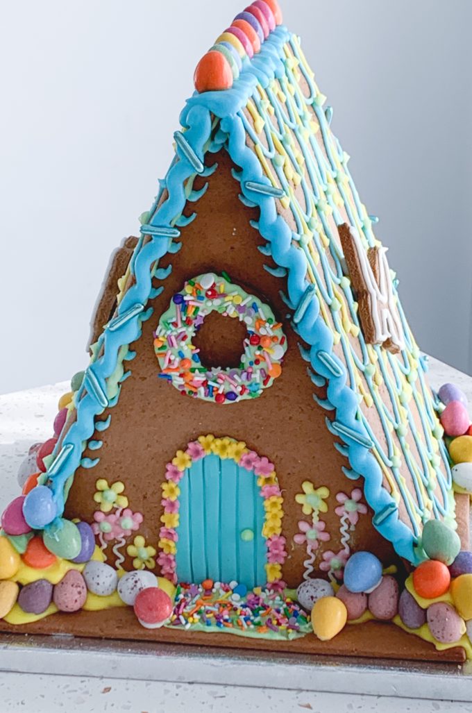 A triangle Easter gingerbread house decorated in sweets, bright colours and lots of chocolate eggs