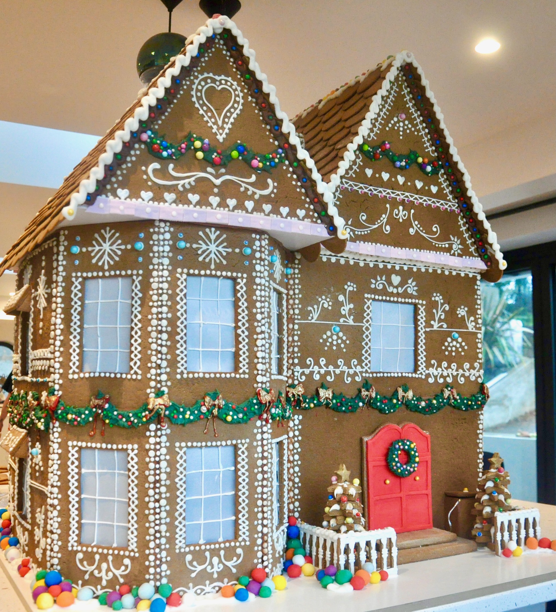 A huge 3ft tall gingerbread house with red front door and lots of intricate piping over the front