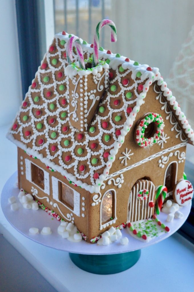 red green and gold traditional gingerbread house on a stand