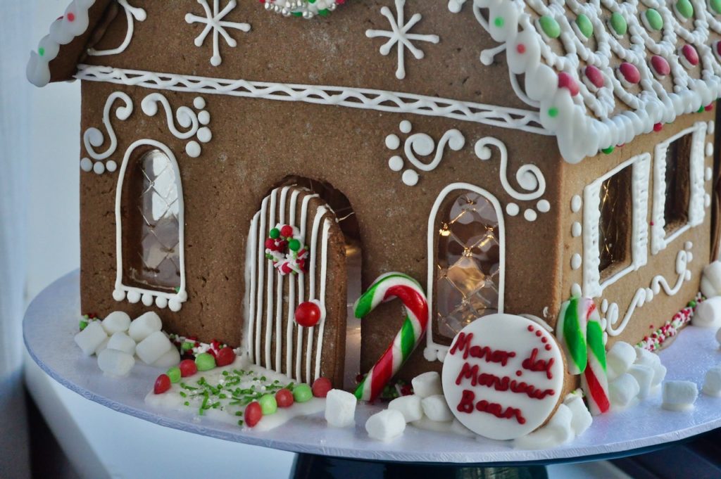 Close up of the front of a red and green gingerbread house with royal iced door, candy canes and decoration