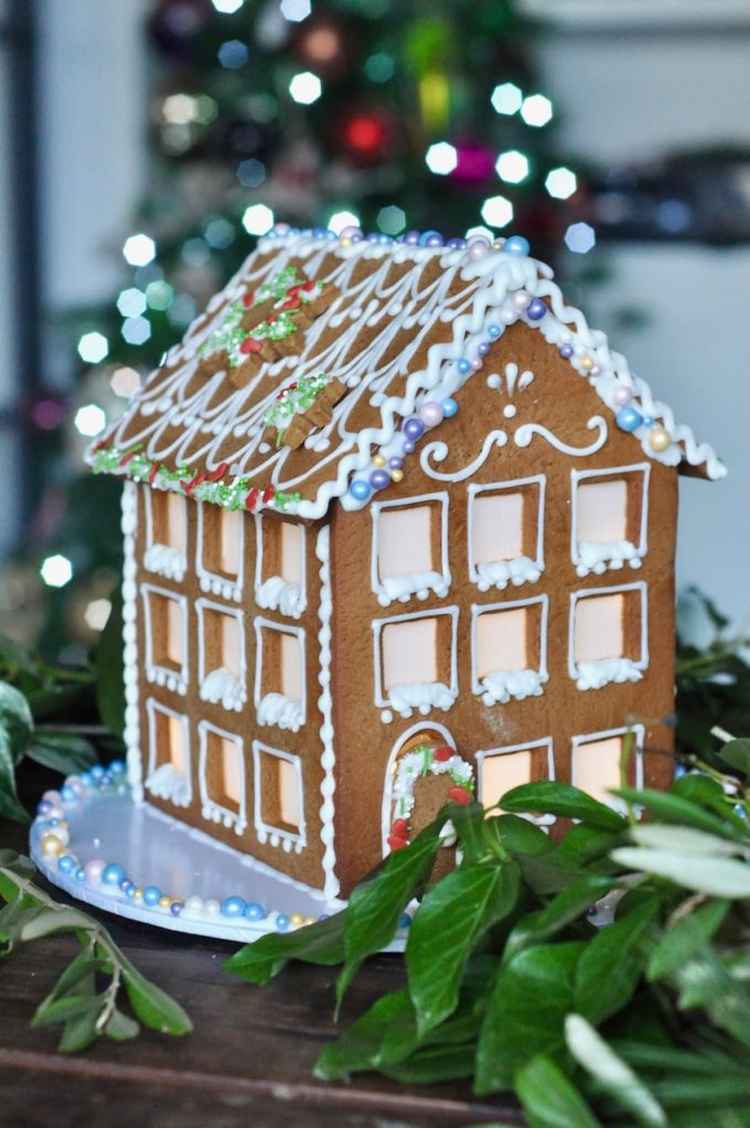 A vgen gingerbread town house with lit up windows and tasty vegan sugar decorations