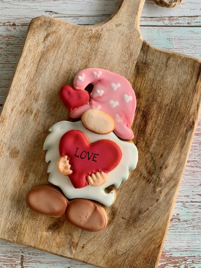 A cookie biscuit ginger puzzle made of four pieces to look like a cute gnome with a pink hat and holding a red heart across its beard